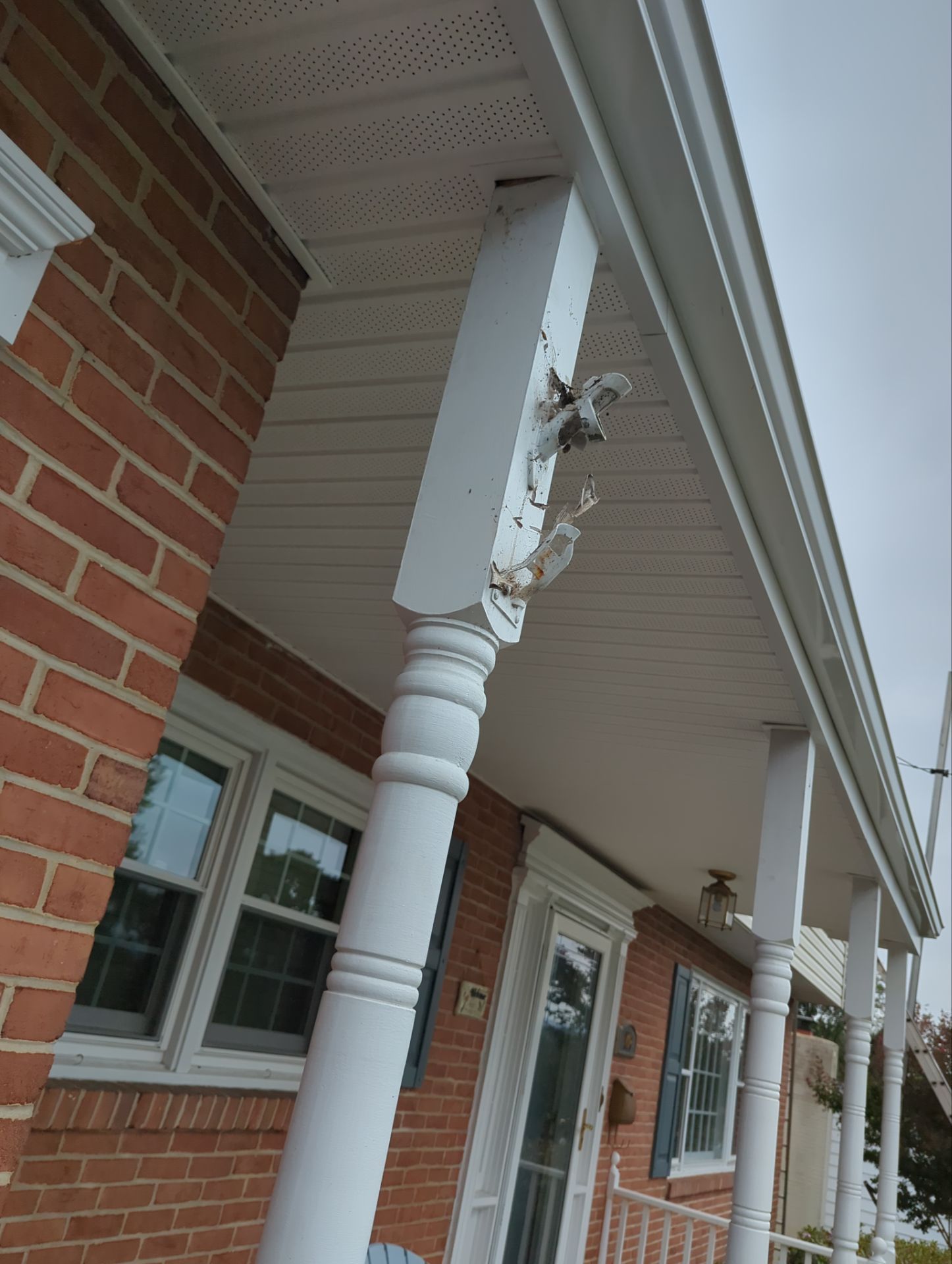 White porch column and trim on a red brick house. Gray sky in the background.