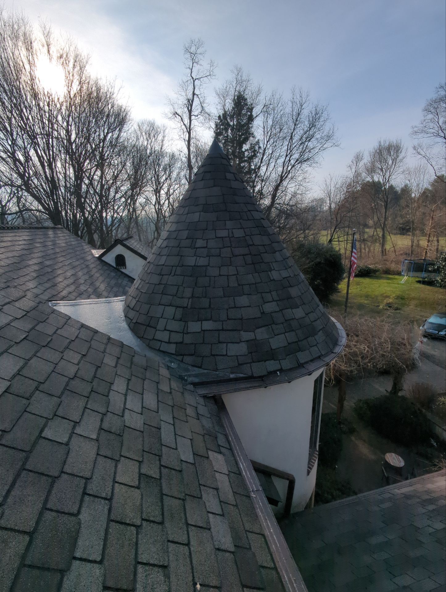 Large beige house with a turret and dark roof, under a cloudy blue sky. A car is in the driveway.