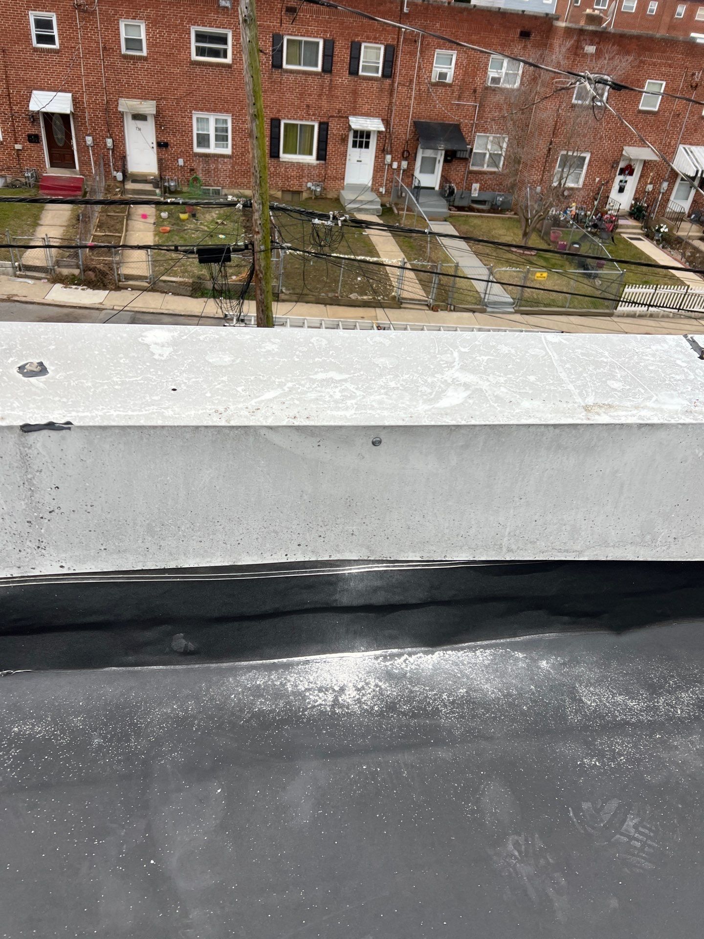 Concrete ledge on a black roof, row houses in background.