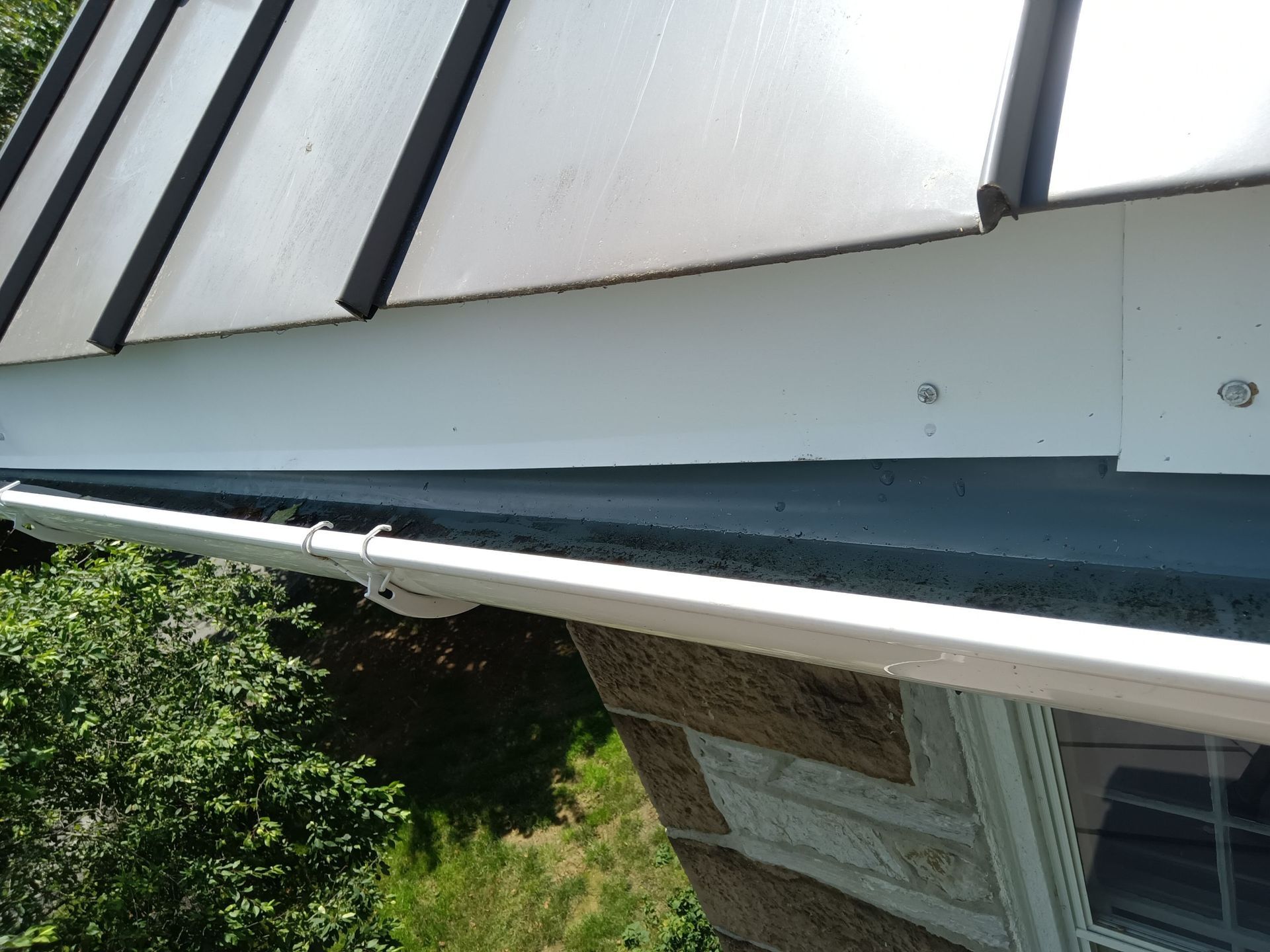 White gutters under a roof with a clear panel; light-colored stone wall.