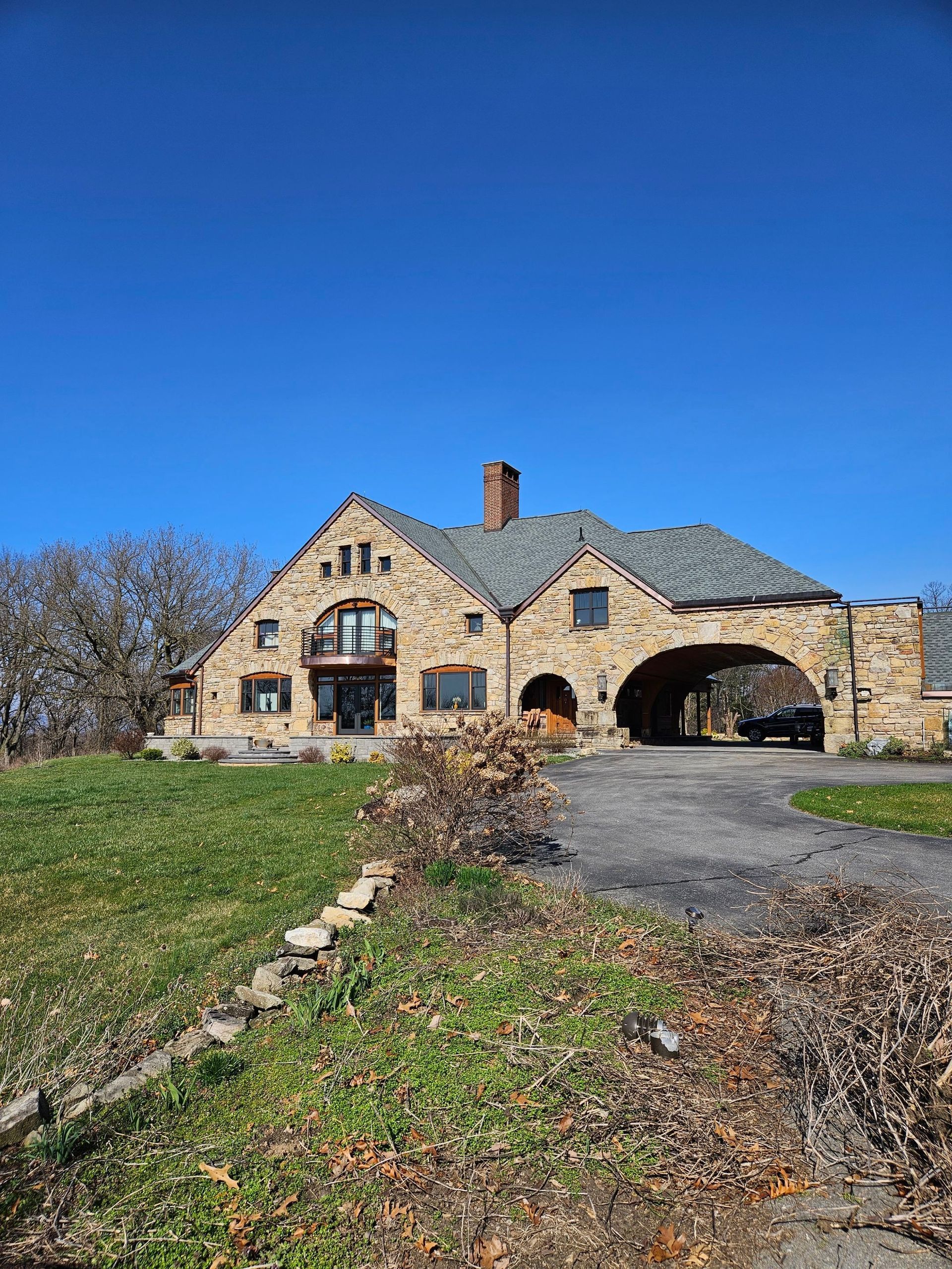 Stone mansion with arched entrance, driveway, and chimney against a blue sky.