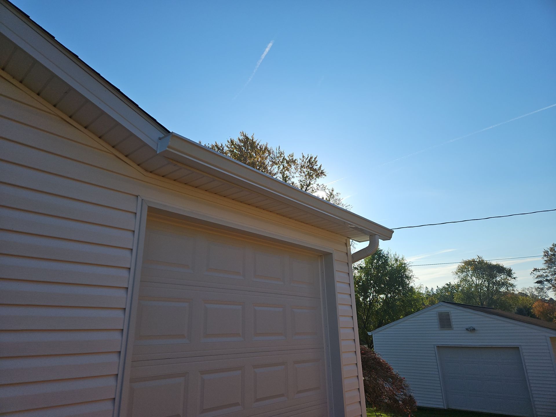 Garage with white siding and door, under a blue sky, with a small detached garage in the background.