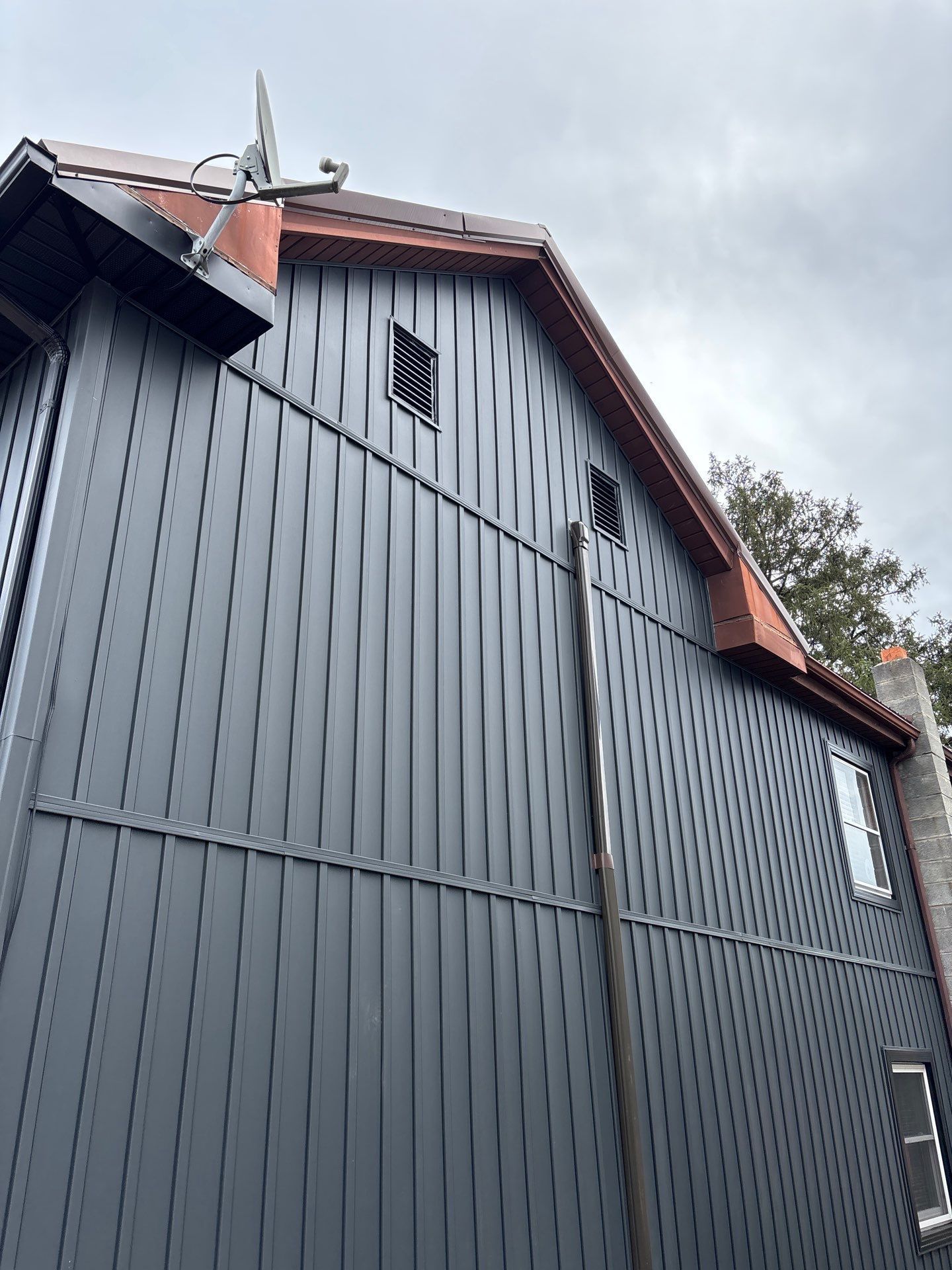Dark gray siding on a building with a red roof under a cloudy sky.