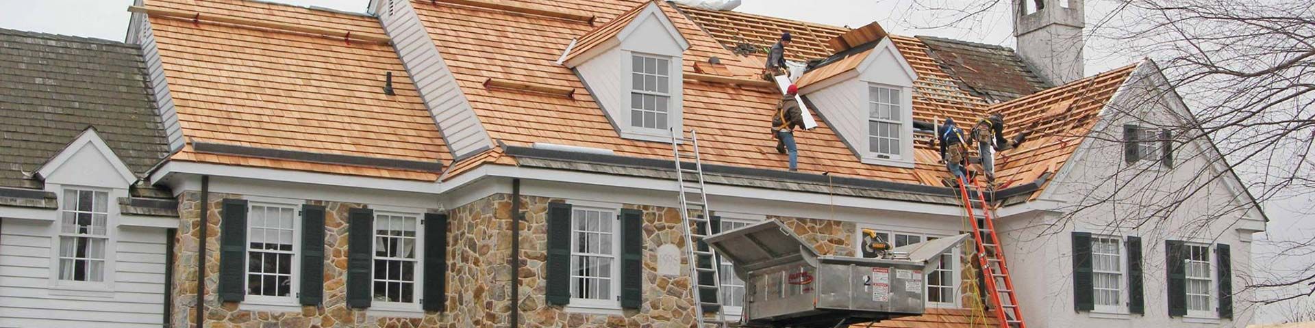 Aerial view of a large, stone house with cedar shake roof, green lawn, and swimming pool.
