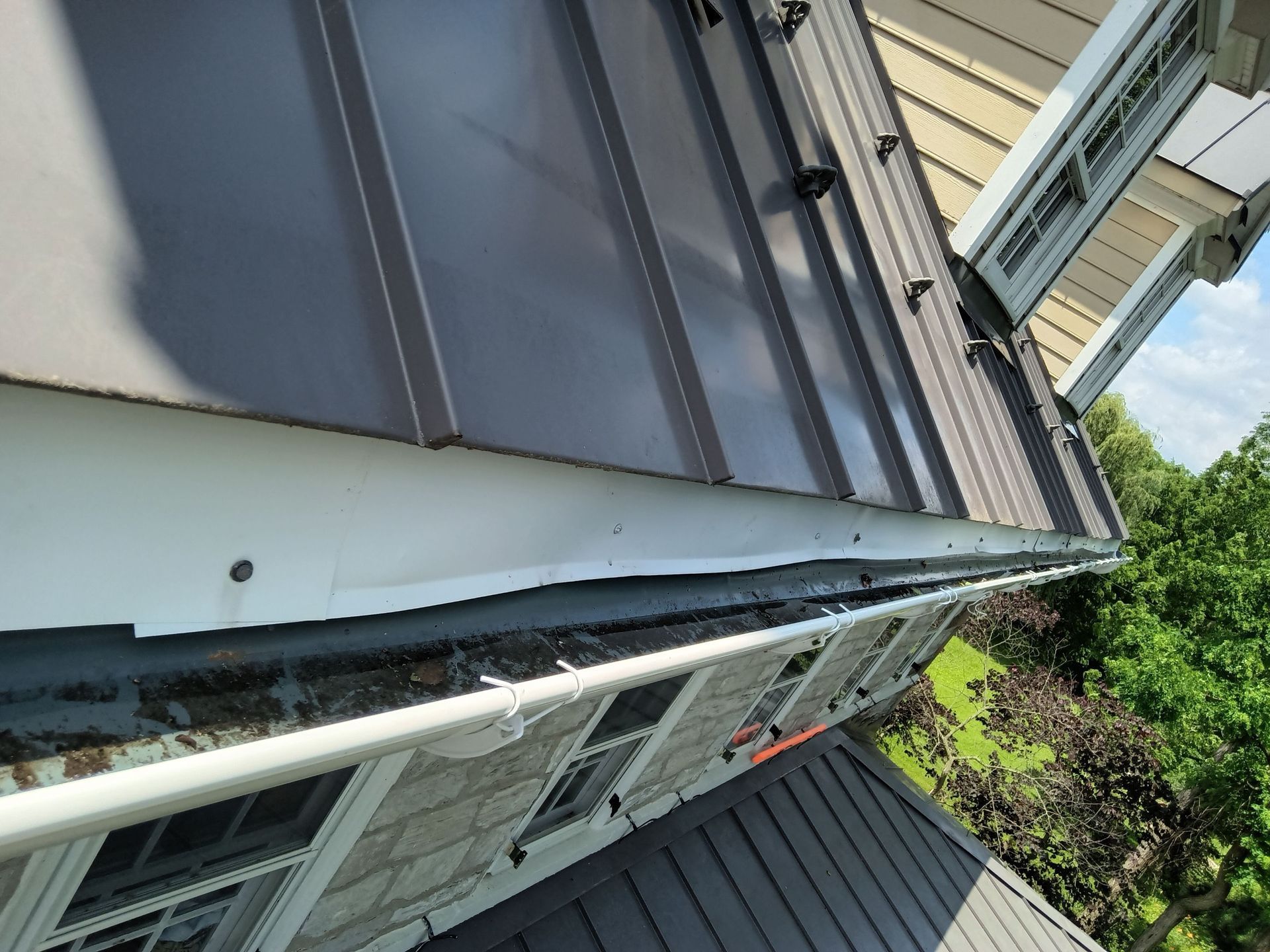 Dark metal roof with gutter and white trim on a house exterior.