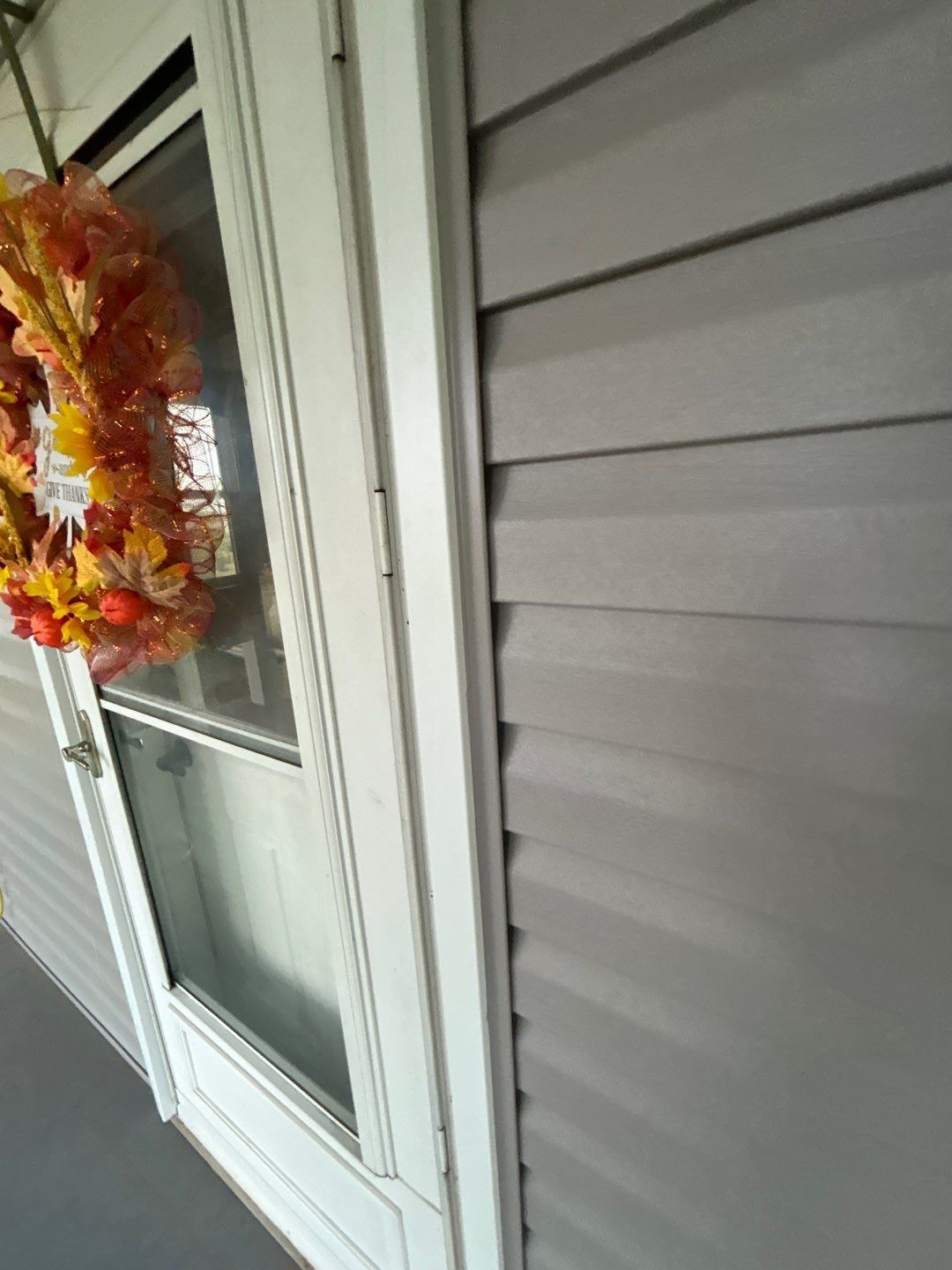 Door with white trim, gray siding, and a fall wreath.