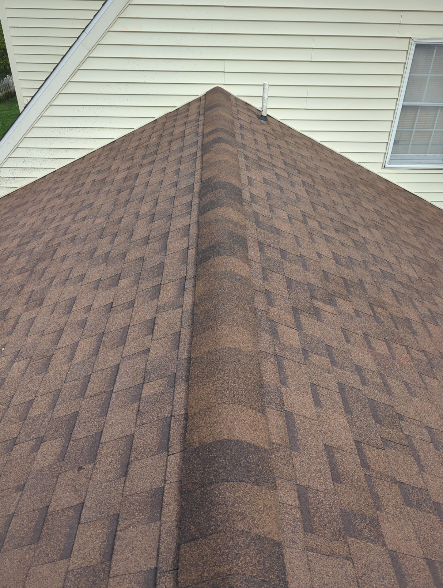 Brown shingle roof with a central ridge, against a tan house exterior and a window.