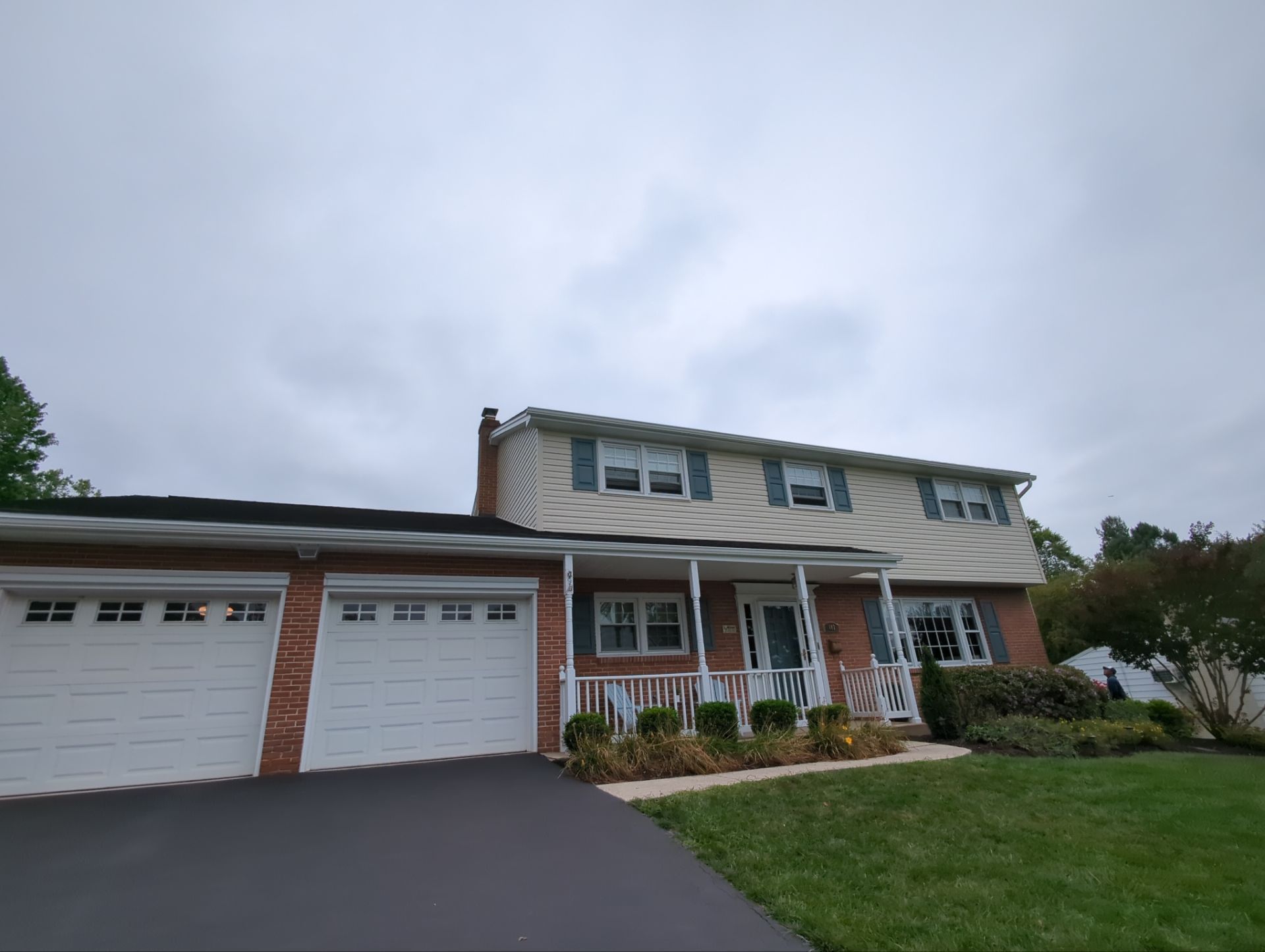 Two-story house with a brick facade, white garage doors, and a front porch under a cloudy sky.