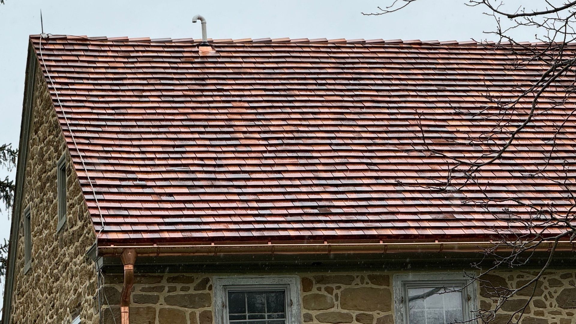 Red tiled roof on a stone building with two windows.