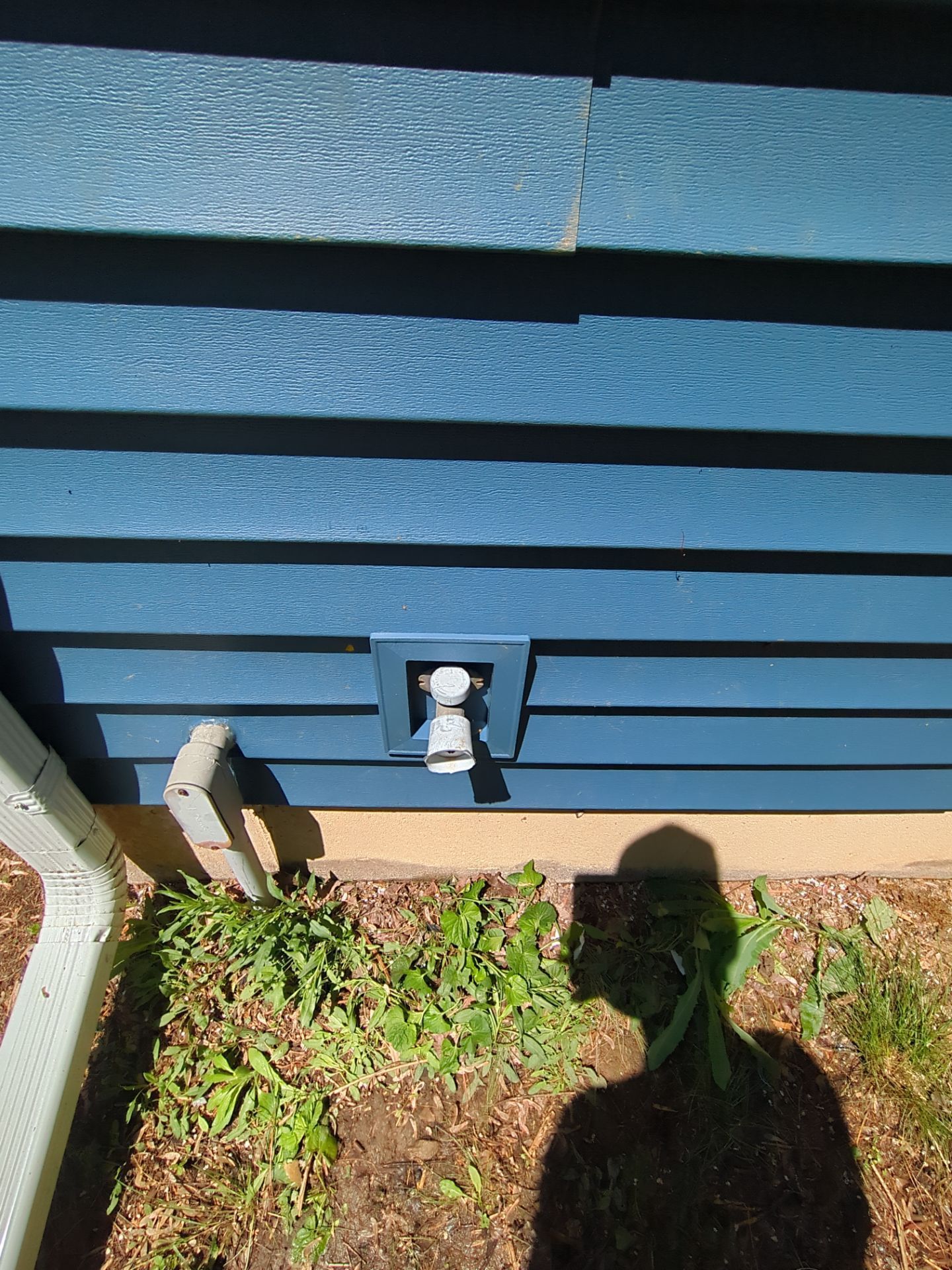 Blue siding with a water spigot and shadow of a person.