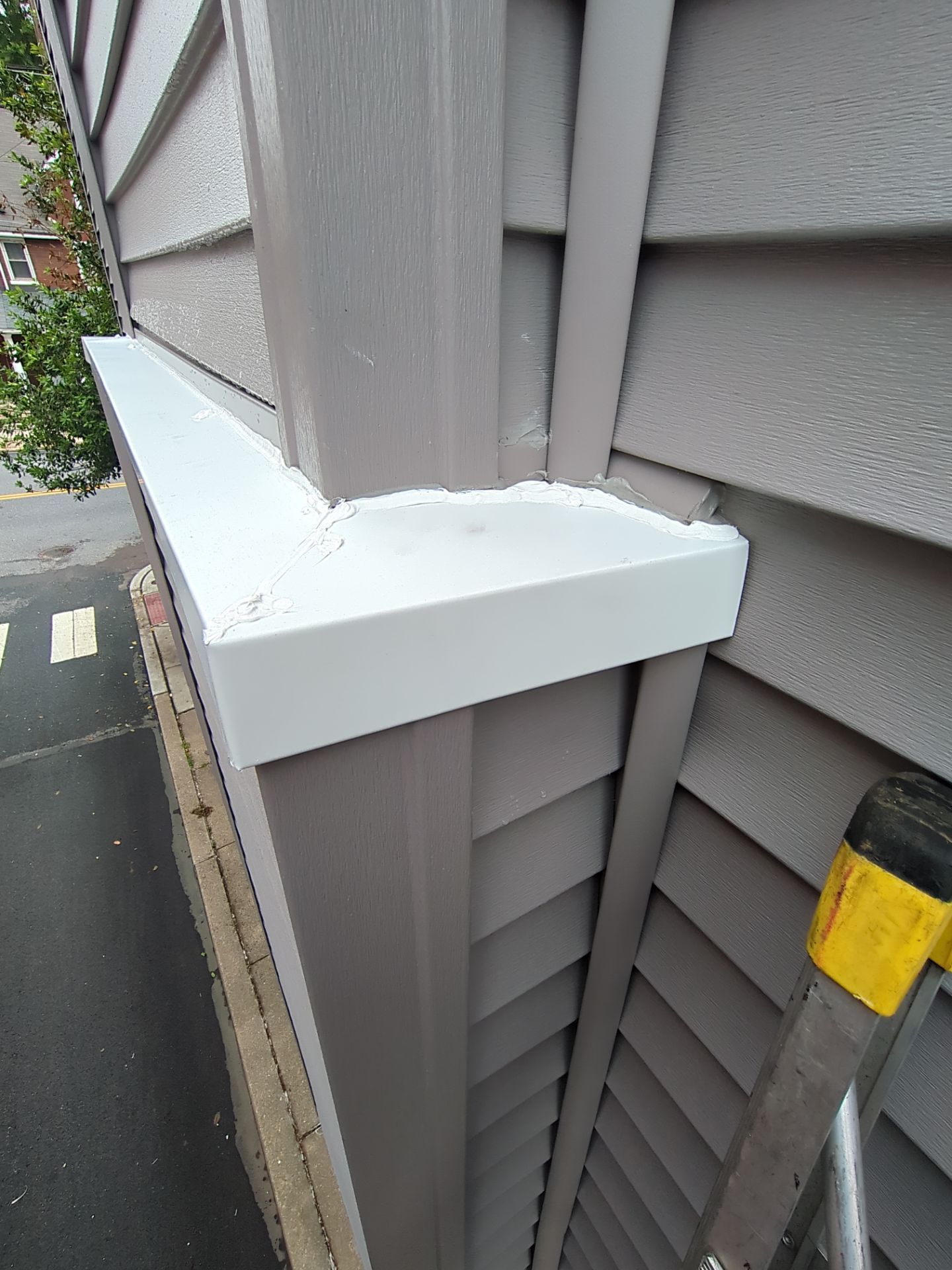 White trim along a building corner, next to gray siding. A ladder leans against the siding.
