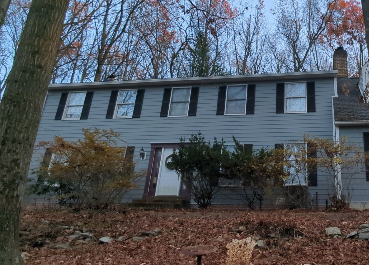 Stone house with arched entryway, balcony, and garage; trees in background.