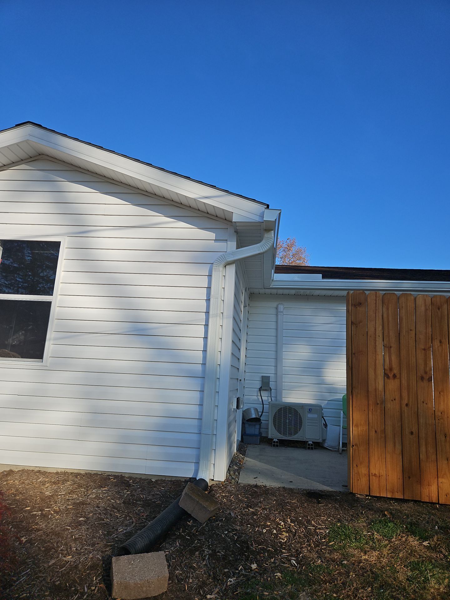 White house exterior with air conditioner unit, brown fence, and blue sky.