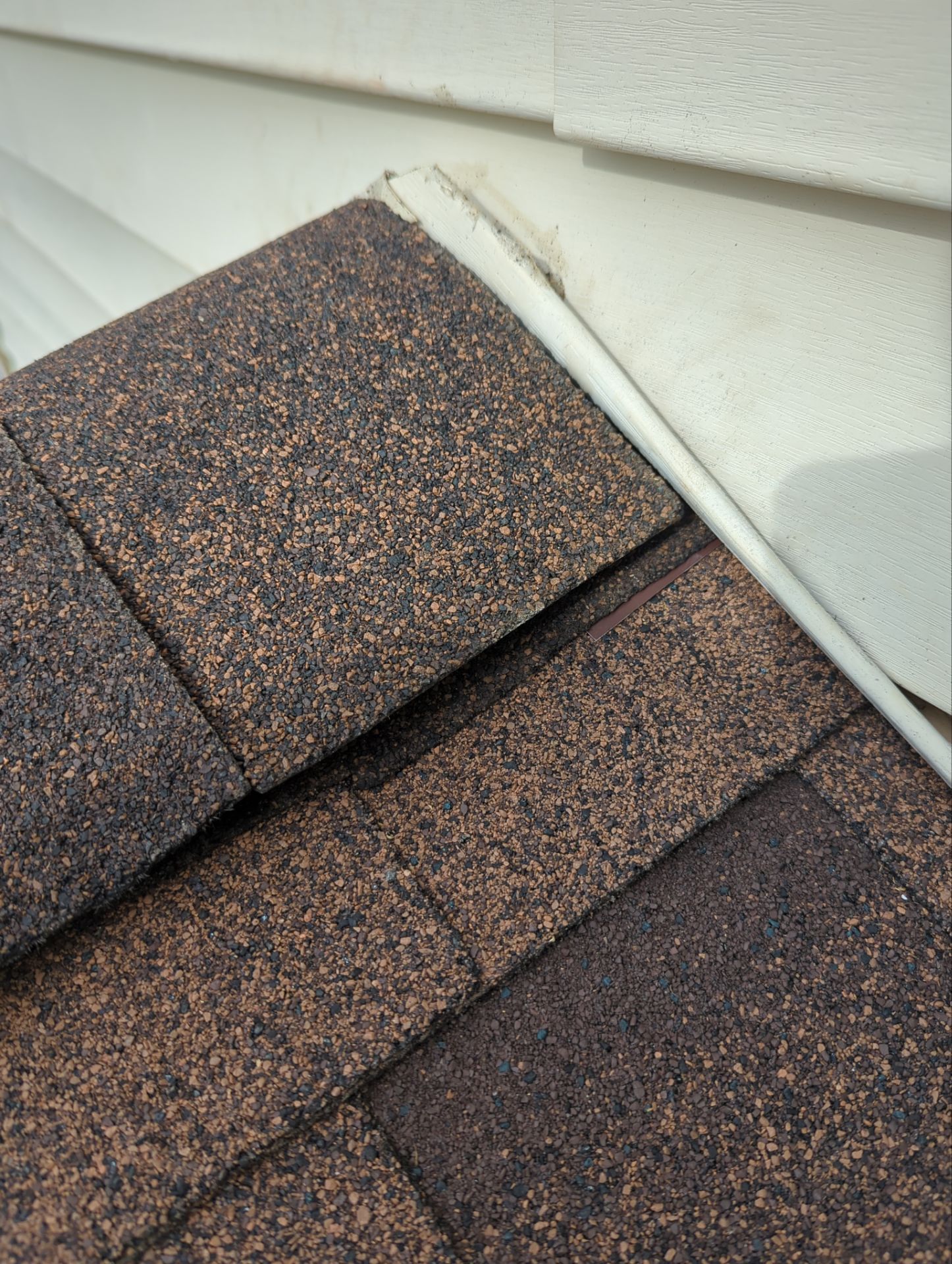 Close-up of brown asphalt roof shingles meeting white siding.