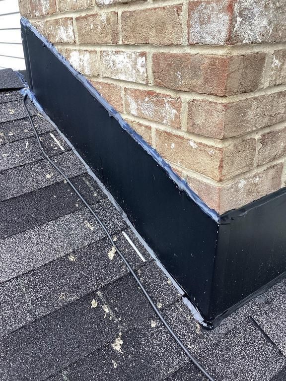Black flashing seals around a brick chimney on a shingled roof.