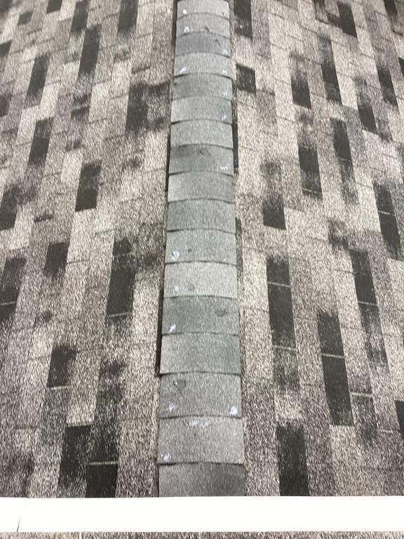 View of a roof ridge with overlapping gray asphalt shingles and ridge cap shingles.