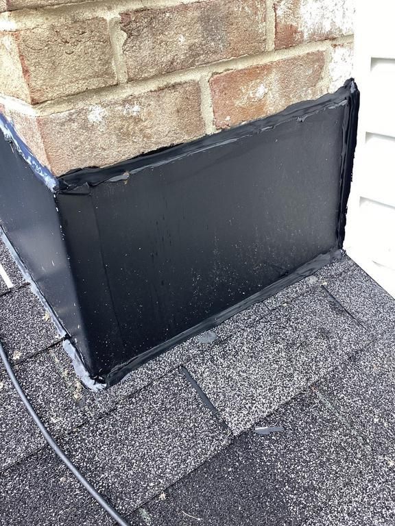Black metal flashing on a brick chimney where it meets the roof shingles.