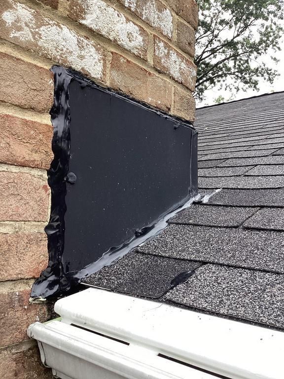 A chimney flashing repair with black sealant on a brick chimney and asphalt shingle roof.
