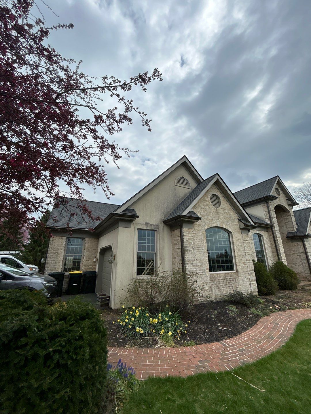 A beige house with arched windows, brick pathway, and cloudy sky overhead.