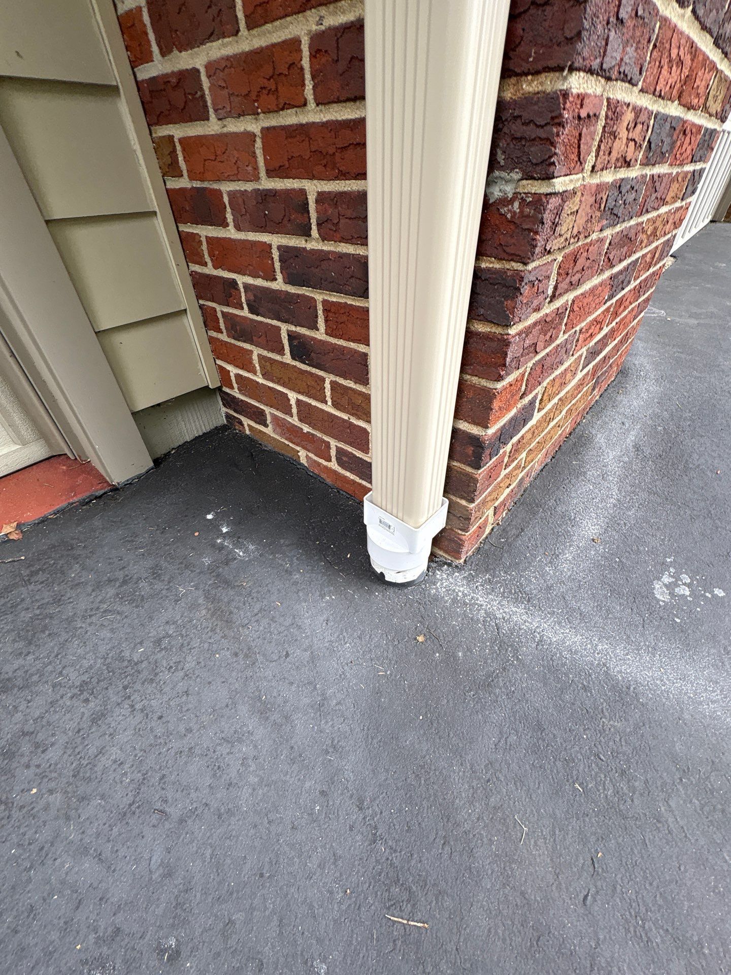 Tan gutter and downspout against a brick building on a dark pavement.