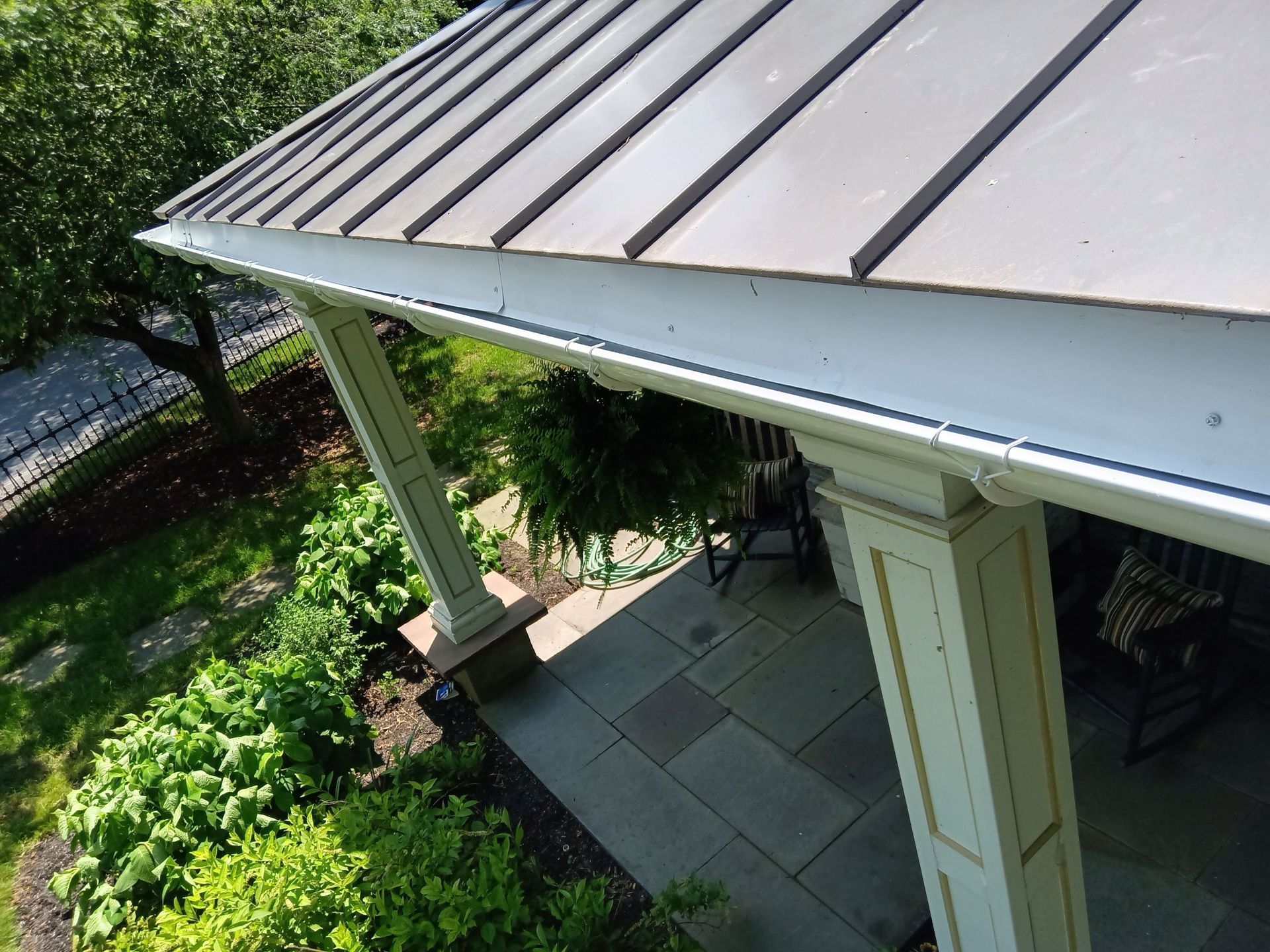 Porch with metal roof and white trim, overlooking a stone patio and garden.