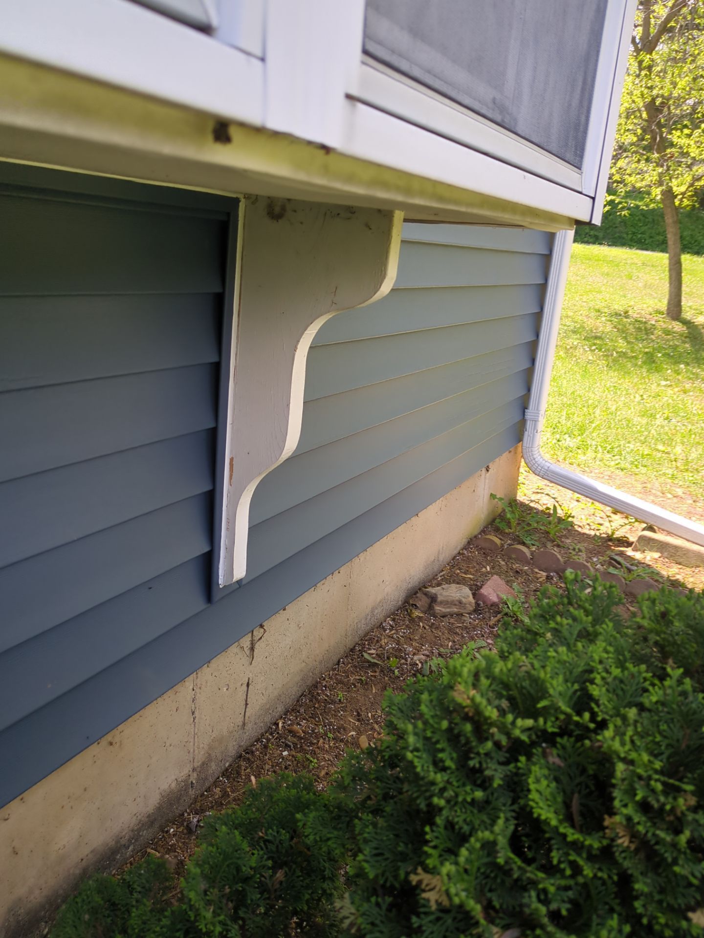 Gray siding with a decorative bracket under a window.
