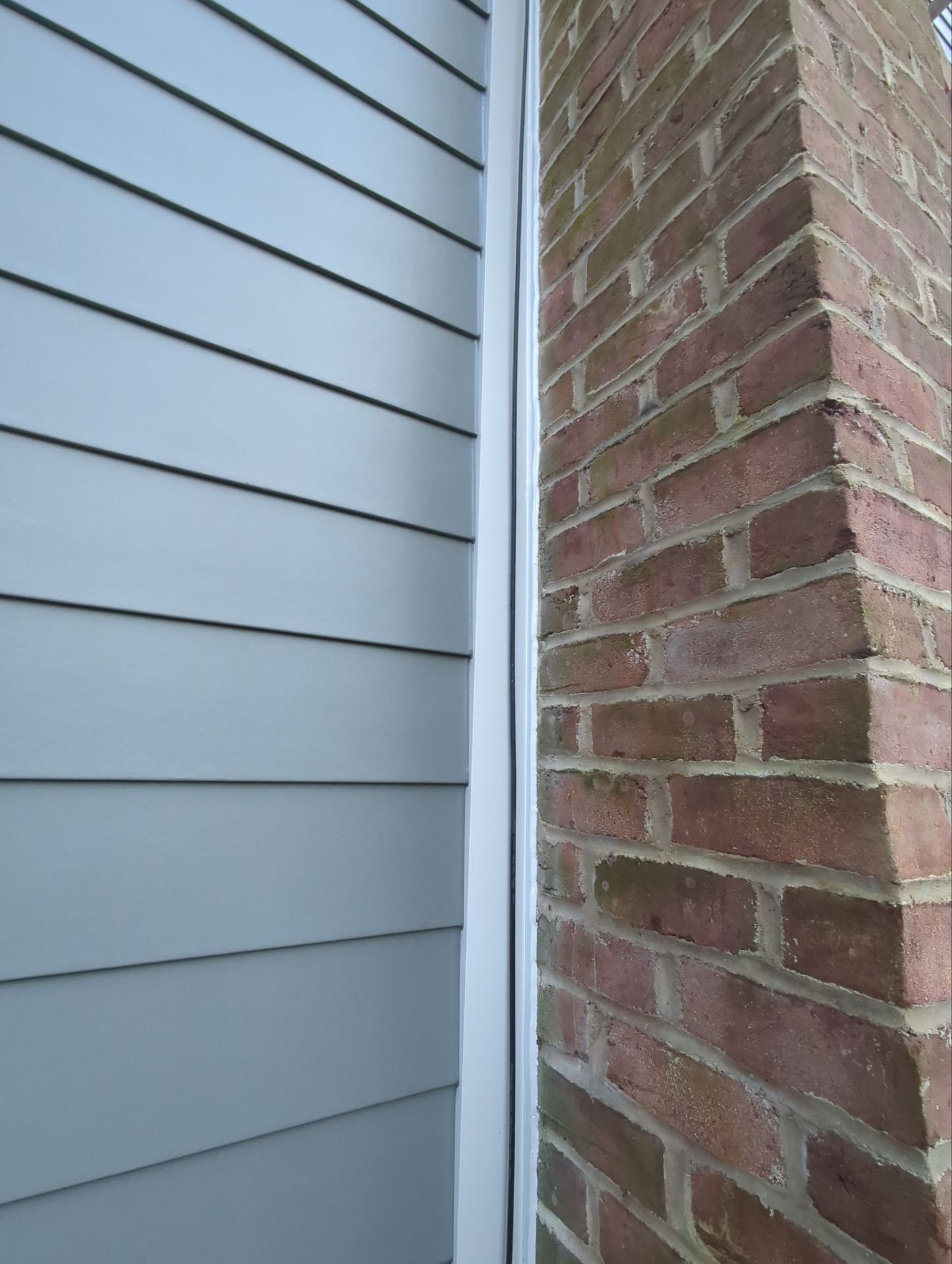 Blue siding next to a brick chimney with white trim separating them.