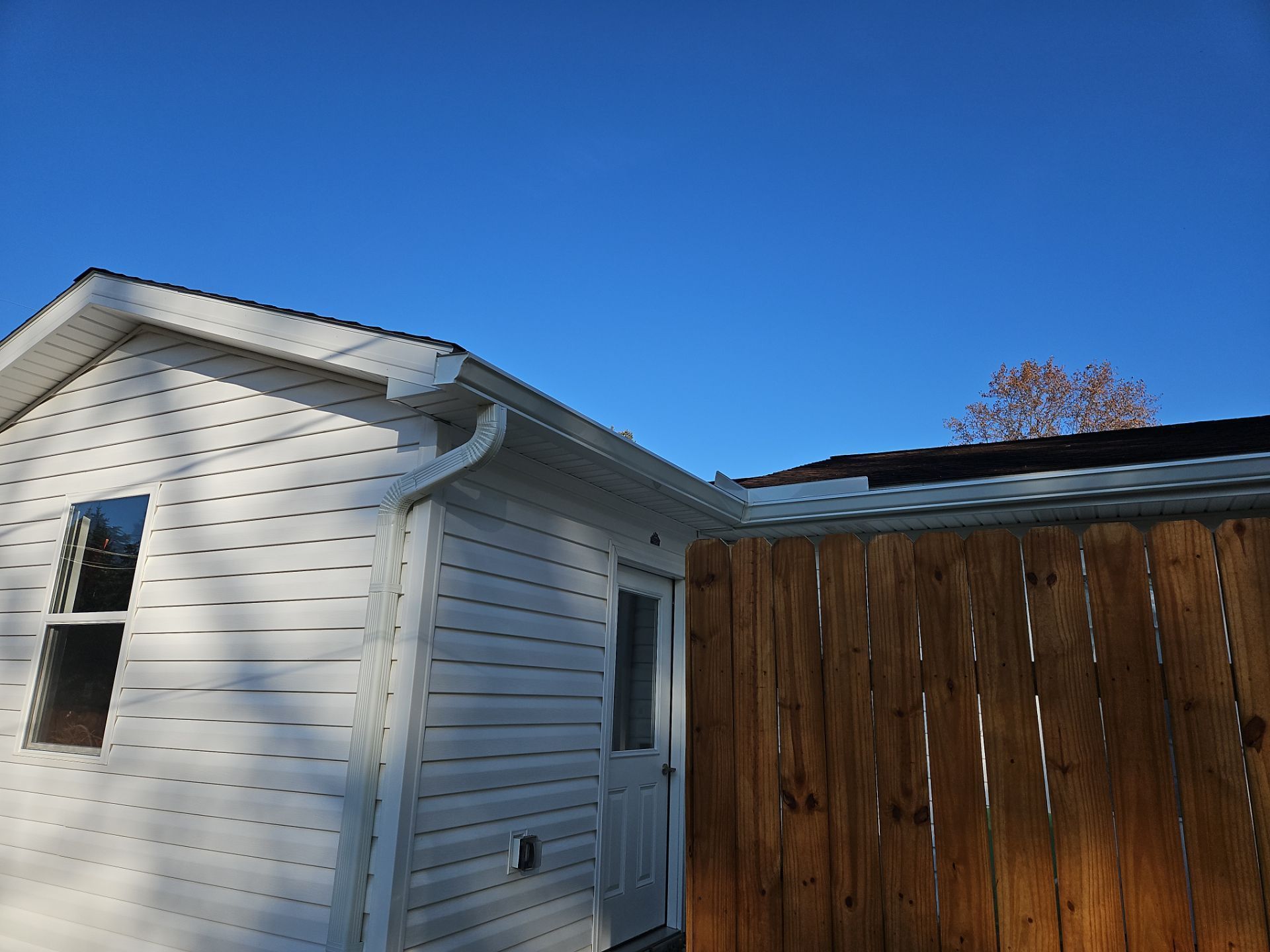 White-sided building with window and door, brown fence, clear blue sky.