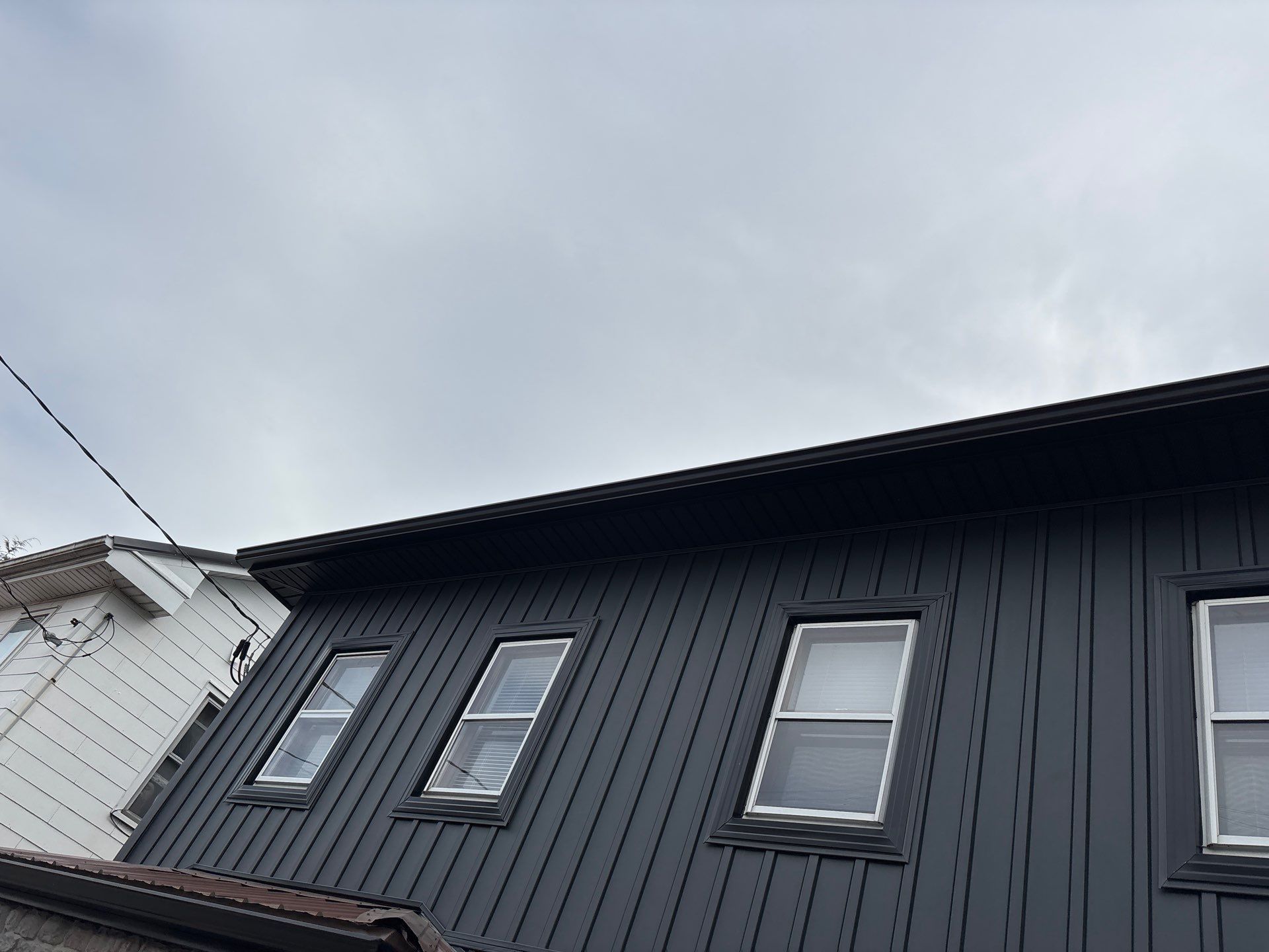 Black-painted building with three rectangular windows under a cloudy sky.