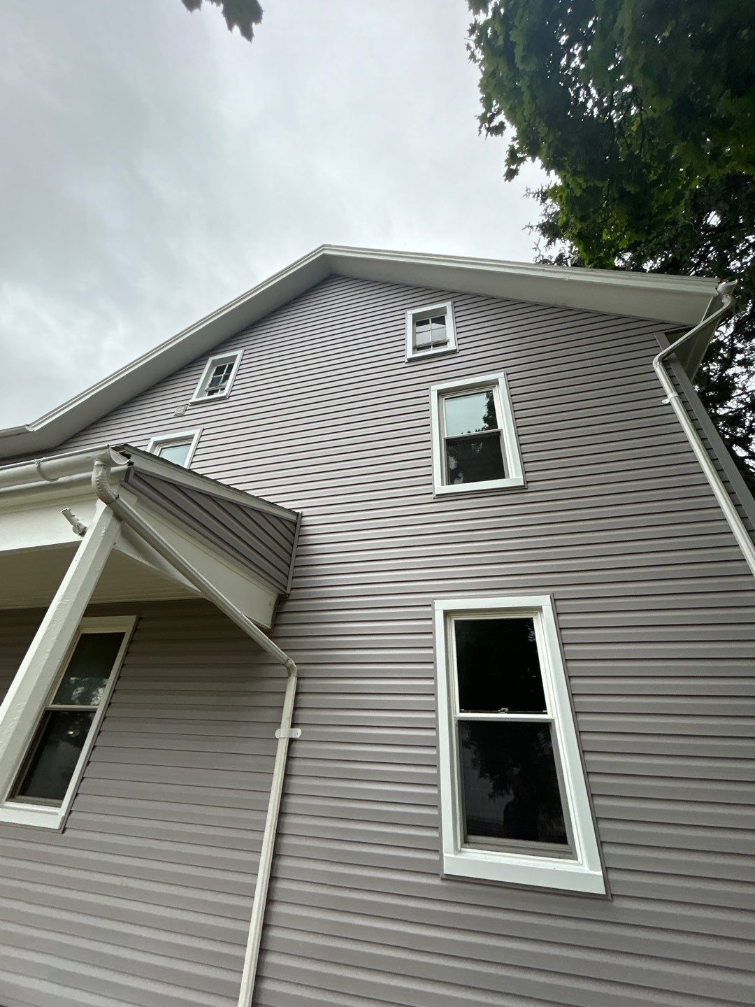 Gray siding on a two-story house with white-framed windows under a cloudy sky.