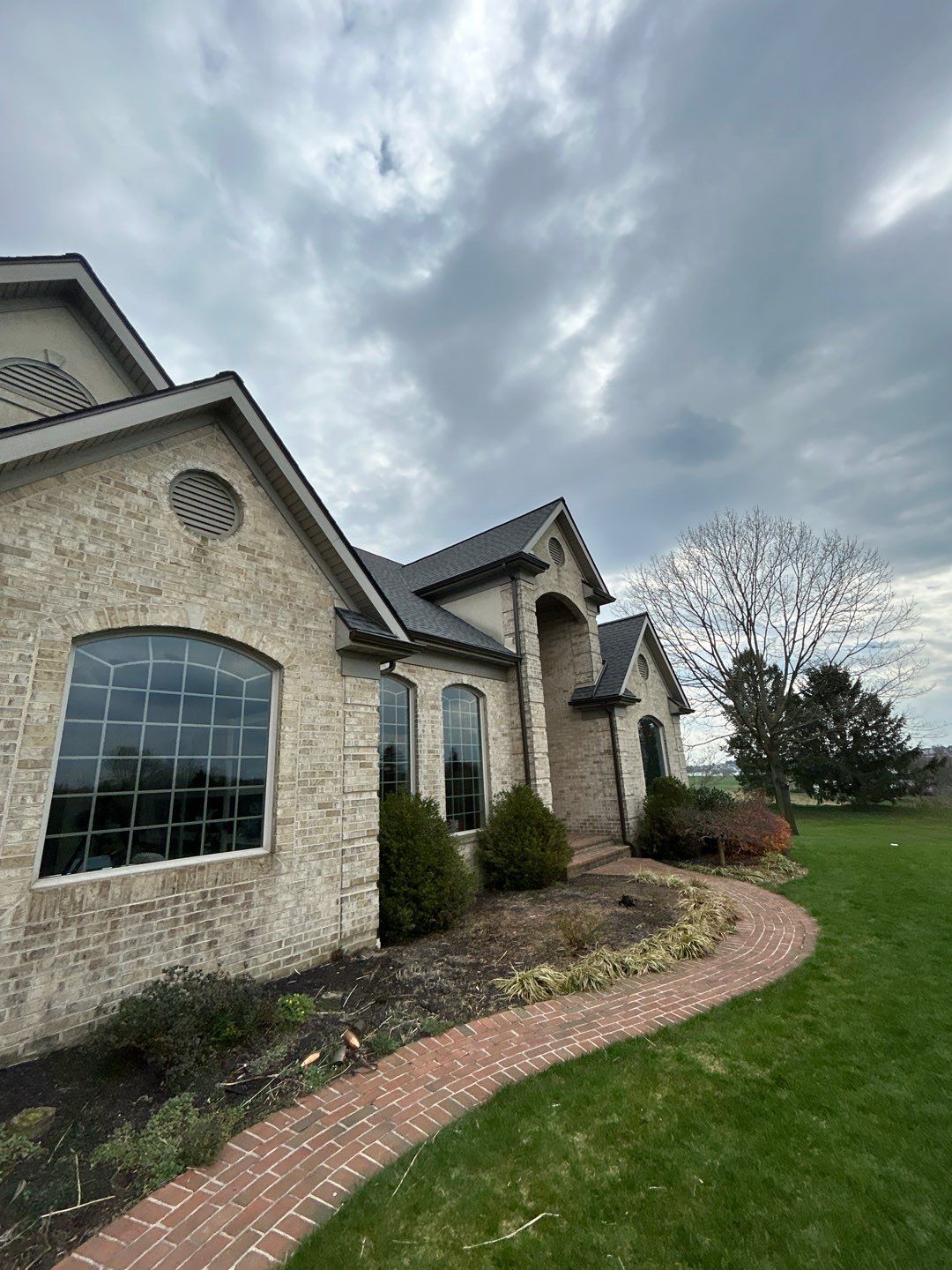 Brick house with dark roof and arched windows; brick pathway winds through grass. Overcast sky.