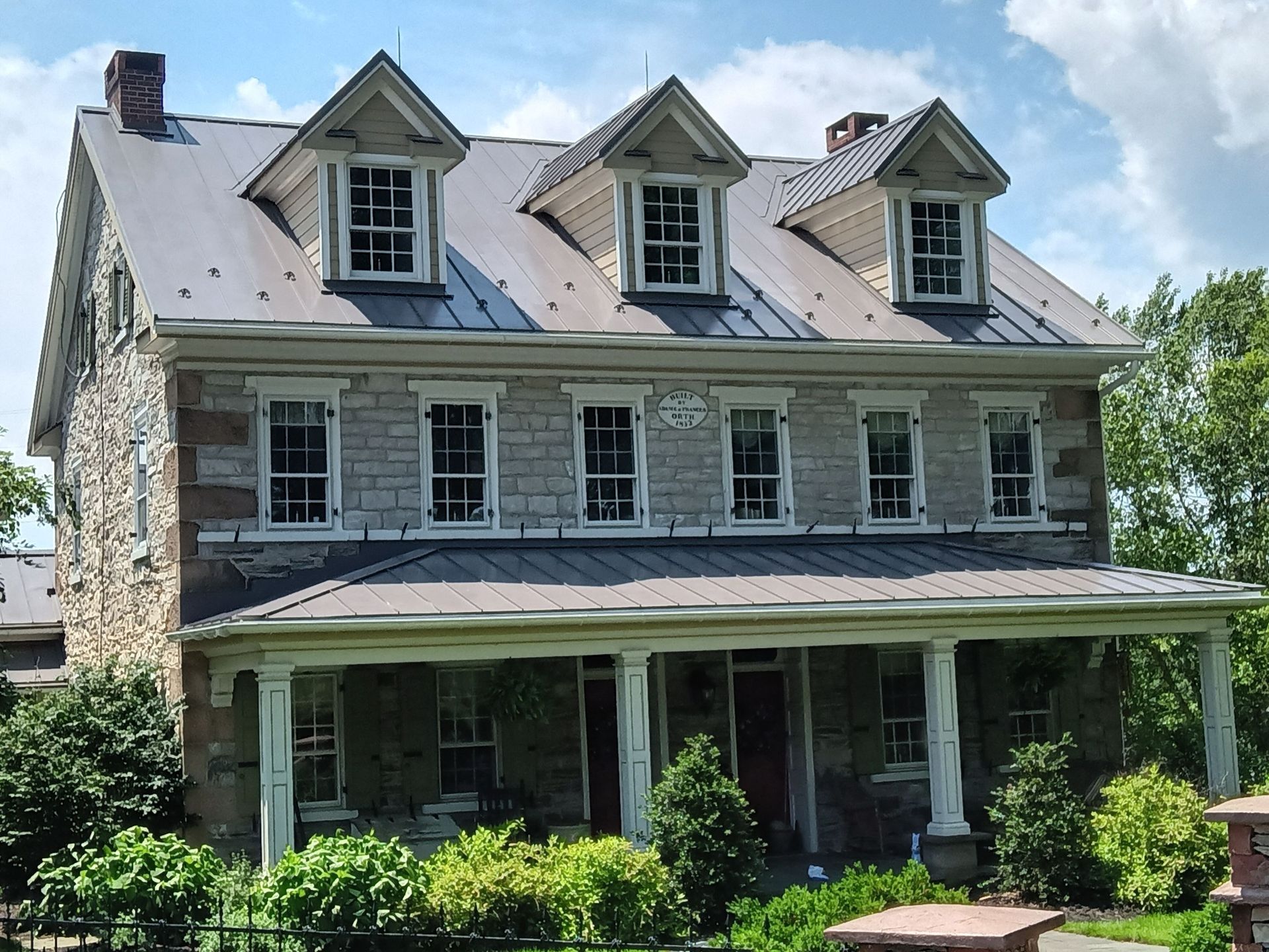 Stone house with three dormers, front porch, and metal roof.