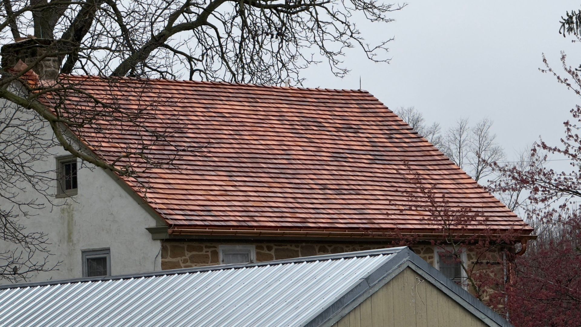 Red tiled roof of a building with visible brick and white walls, trees in background.