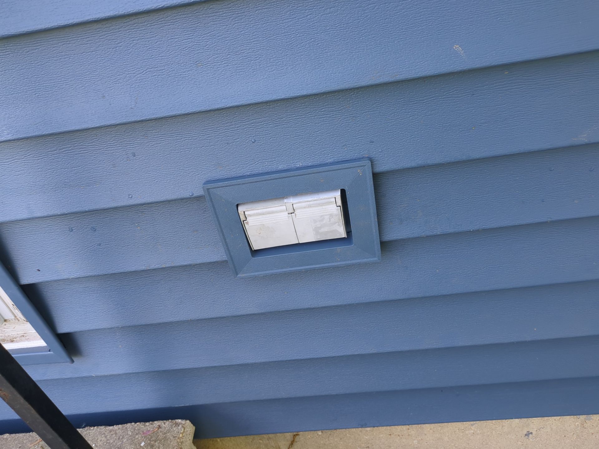 Blue siding with a rectangular vent cover surrounded by a matching frame.