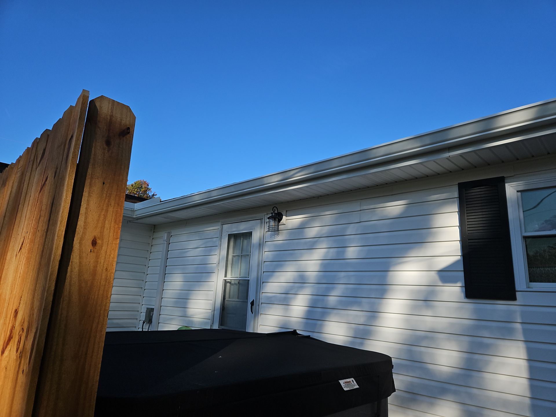Wooden fence in front of a white house with black shutters, under a clear blue sky.
