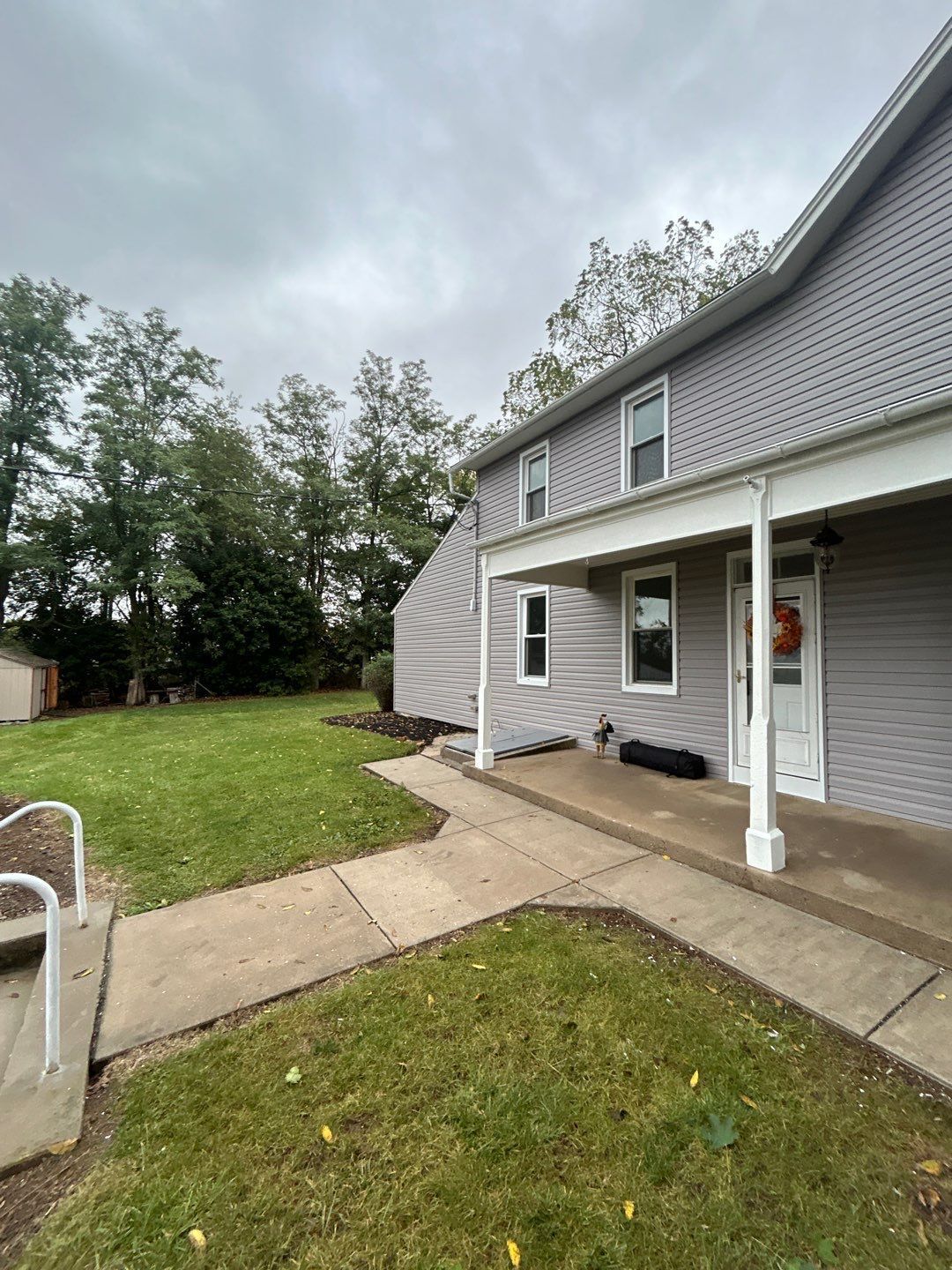 Two-story house with gray siding, porch, and a grassy yard under a cloudy sky.