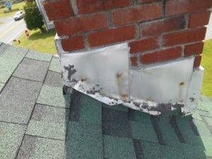 Chimney flashing on a shingled roof, showing rust and damage to the metal.