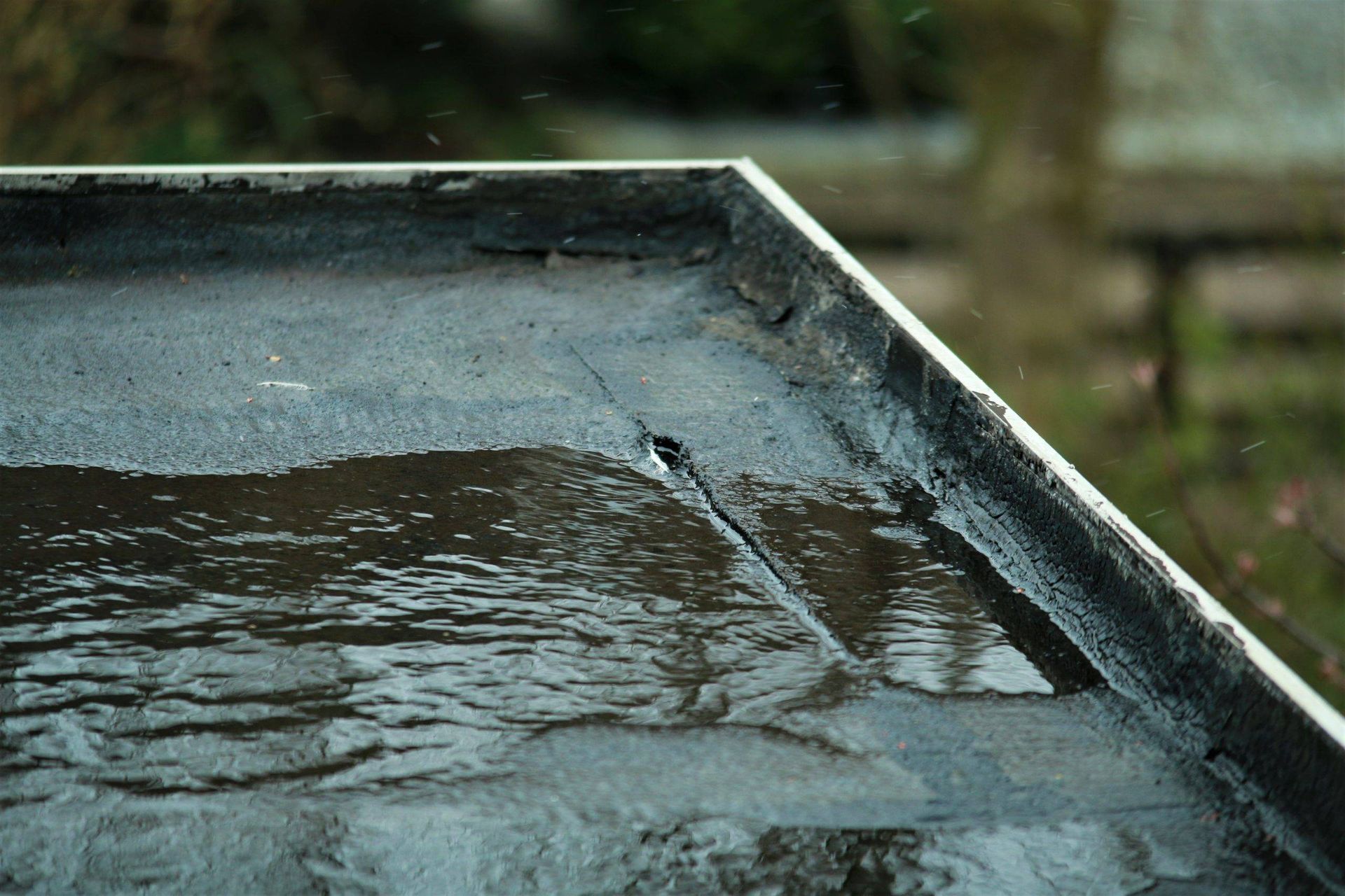 Close-up of a flat, asphalt roof with water pooling and a visible crack.