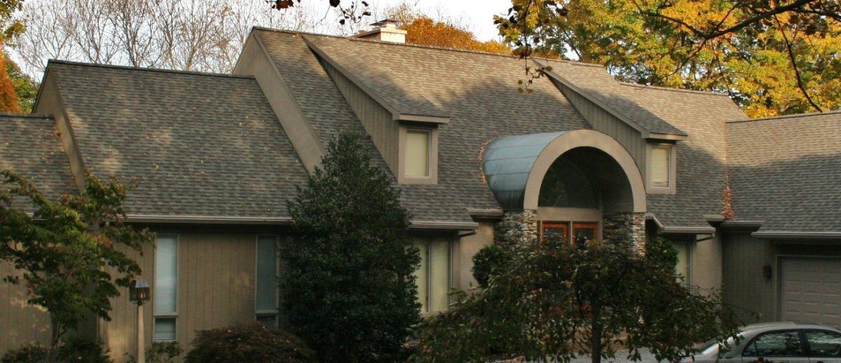 House with a gray roof and light-colored walls; surrounded by trees with fall foliage.
