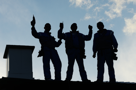 Silhouetted figures on a rooftop celebrate, raising arms. A chimney is at the left, sky is in the background.