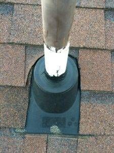 Black rubber pipe flashing on a brown shingle roof, sealed around a vertical pipe.