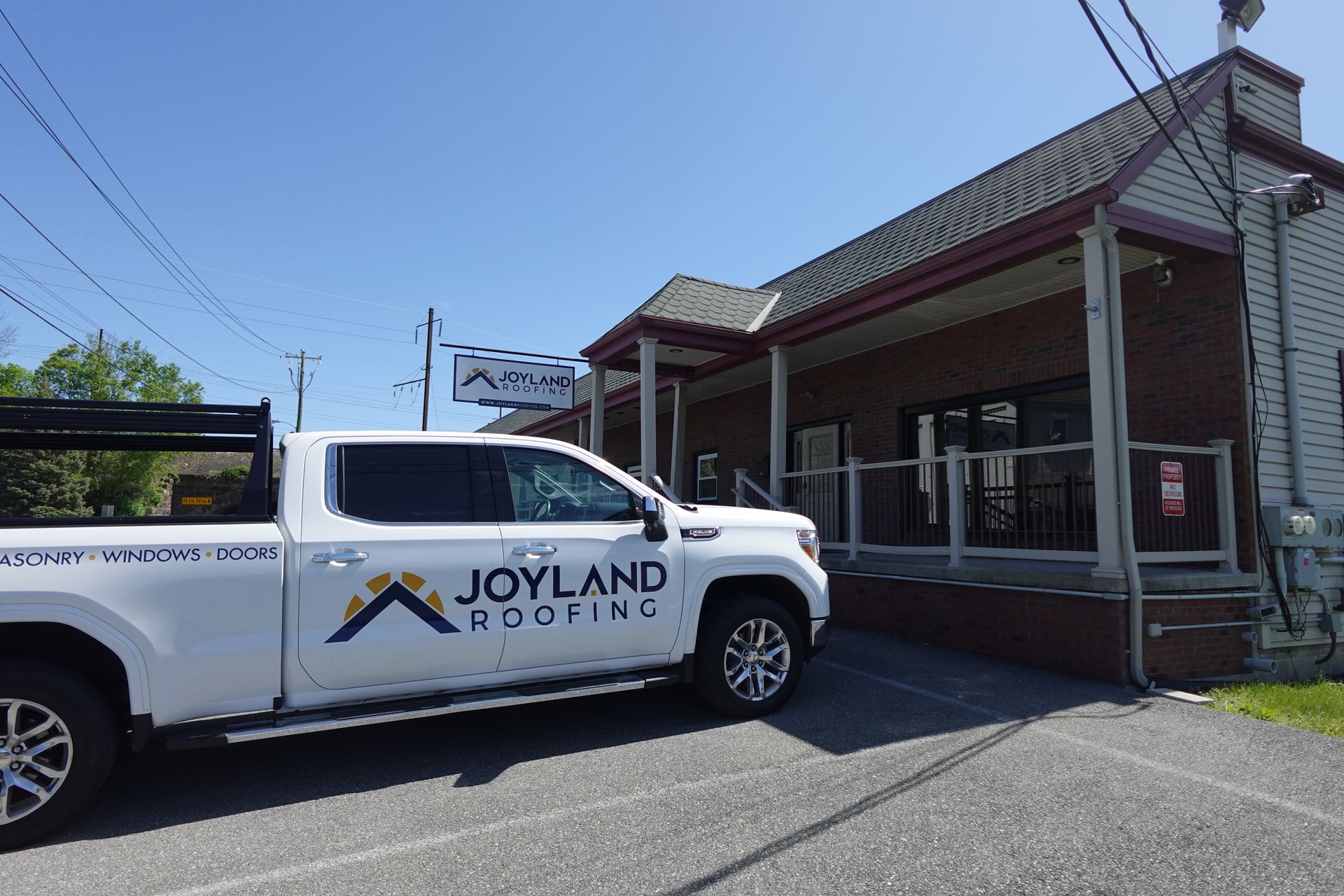 White Joyland Roofing truck parked in front of a brick building on a sunny day.