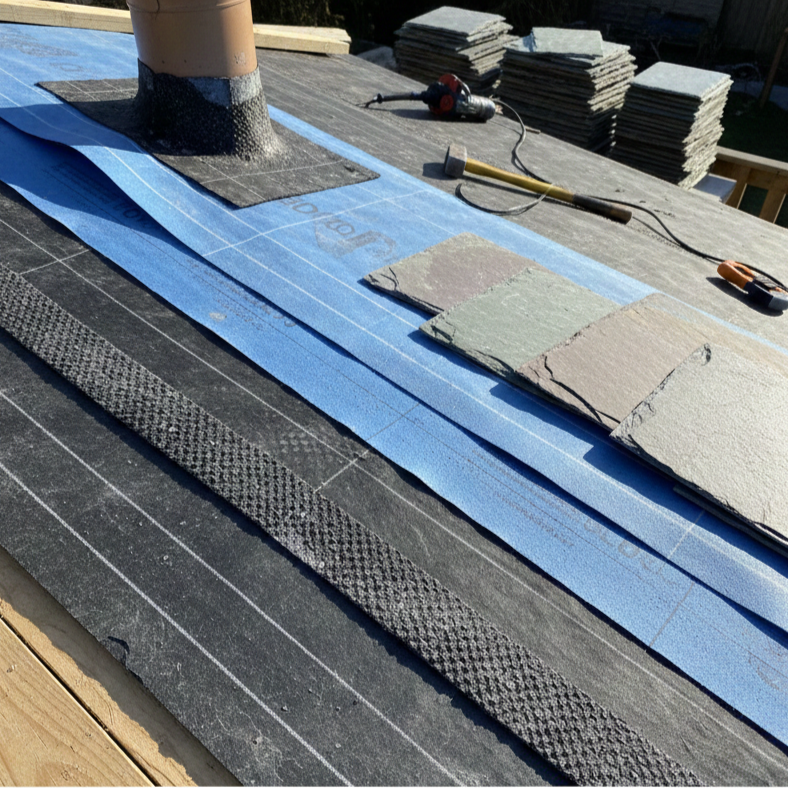 Man in safety vest installing a gray building material on a rooftop, with a close-up view.