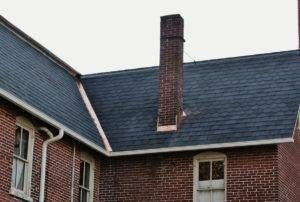 Brick building with blue roof, white gutters, and a tall chimney.