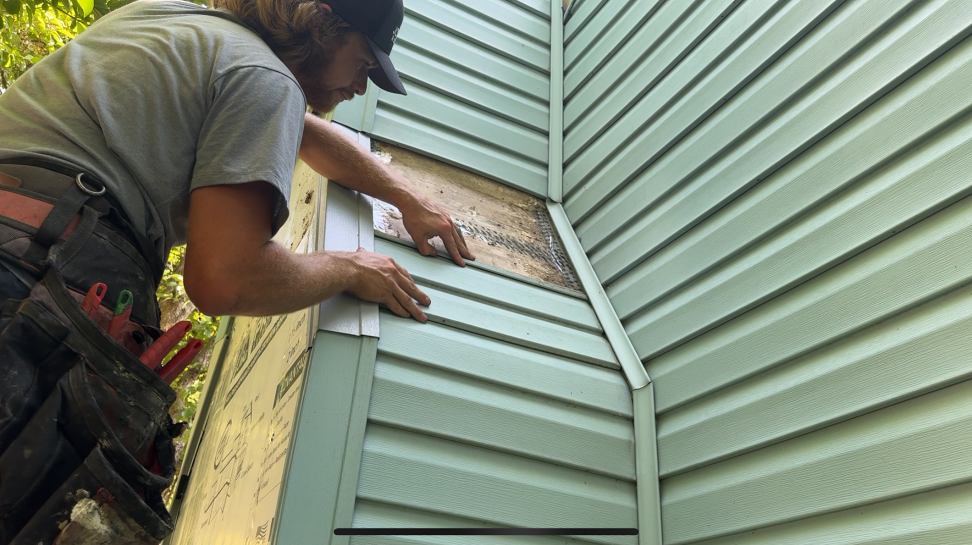 Man in hat installing siding on a corner of a house.