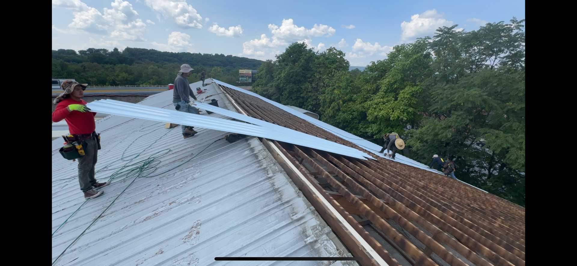 Roofers installing roofing panels on a building. Blue sky and trees in background.