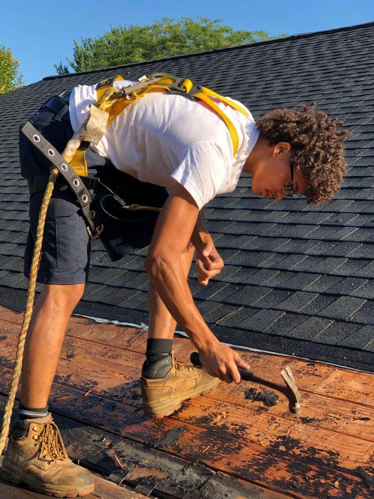Person on a roof using a hammer. They are wearing safety gear and work boots.