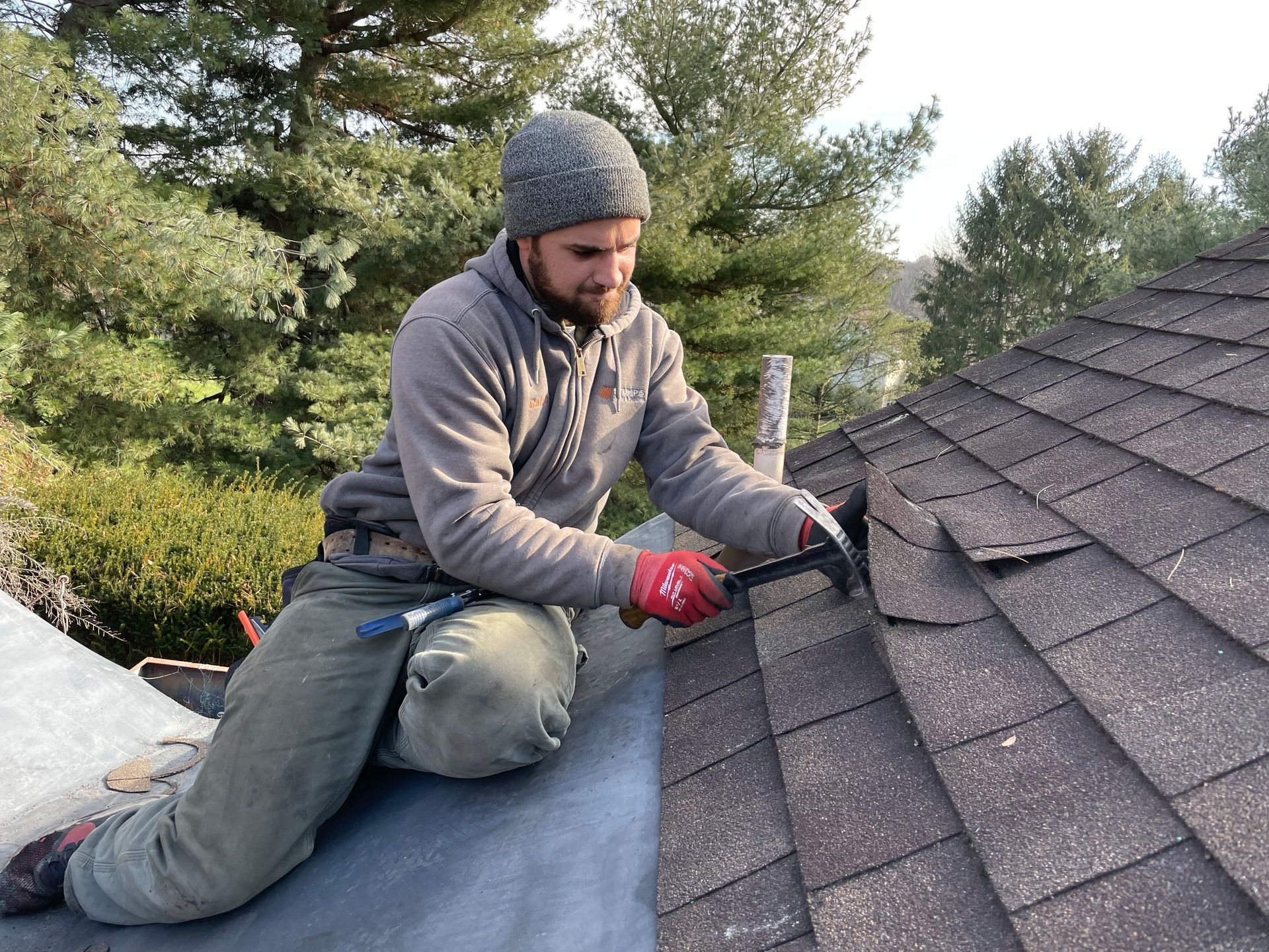 Stone house with a partially replaced cedar shake roof on a sunny day with green grass and trees.