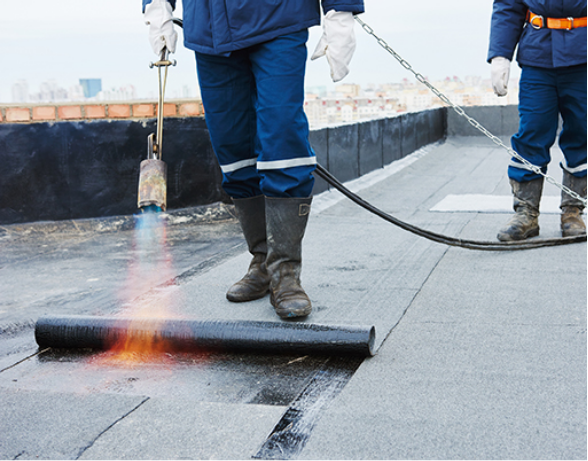 Workers using a torch to install roofing material on a flat roof.