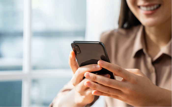 Woman smiling, holding a black smartphone, indoors, blurred background.